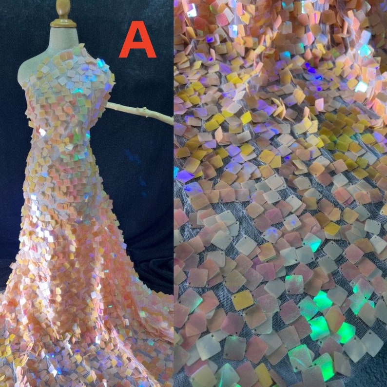 May include: A dress form draped with iridescent fabric. The fabric is covered in small, square sequins in shades of peach, yellow, and white. The sequins catch the light, creating a shimmering effect. The letter "A" is visible in the upper left corner.