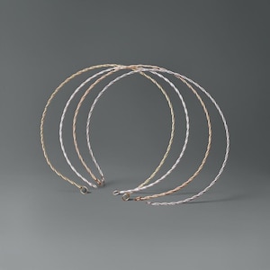 Può includere: Una collezione di cinque cerchietti in filo intrecciato nei toni dell'oro, dell'argento e dell'oro rosa. I cerchietti sono disposti a forma di semicerchio su uno sfondo grigio. Ogni cerchietto ha un piccolo anello all'estremità.