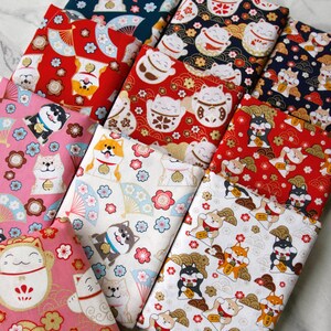 Puede incluir: Varias piezas de tela dobladas con estampados de inspiraci&oacute;n japonesa. Las telas presentan dise&ntilde;os repetidos de gatos de la suerte, perros Shiba Inu, abanicos y motivos florales en colores como rojo, rosa, azul y blanco.