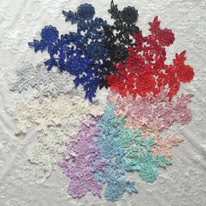 Puede incluir: Una colección de apliques de encaje floral en varios colores, incluyendo blanco, azul, negro, rojo, rosa y morado. Los apliques presentan intrincados diseños florales y de hojas, perfectos para adornar prendas o manualidades.