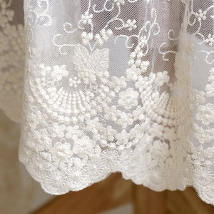 May include: White lace fabric with a delicate floral embroidery pattern. The lace has a scalloped edge.