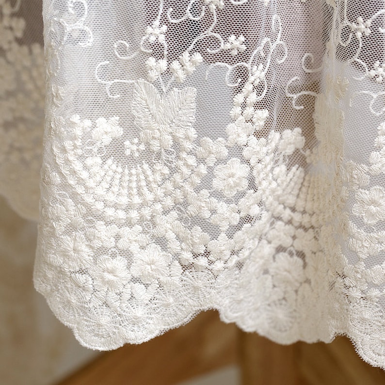 May include: White lace fabric with a delicate floral embroidery pattern. The lace has a scalloped edge.