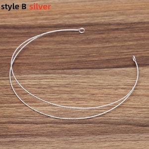May include: Silver-colored necklace with two delicate strands, each with a textured surface. The necklace has a small loop at one end and a hook at the other. The text "style B silver" is in the upper left corner.