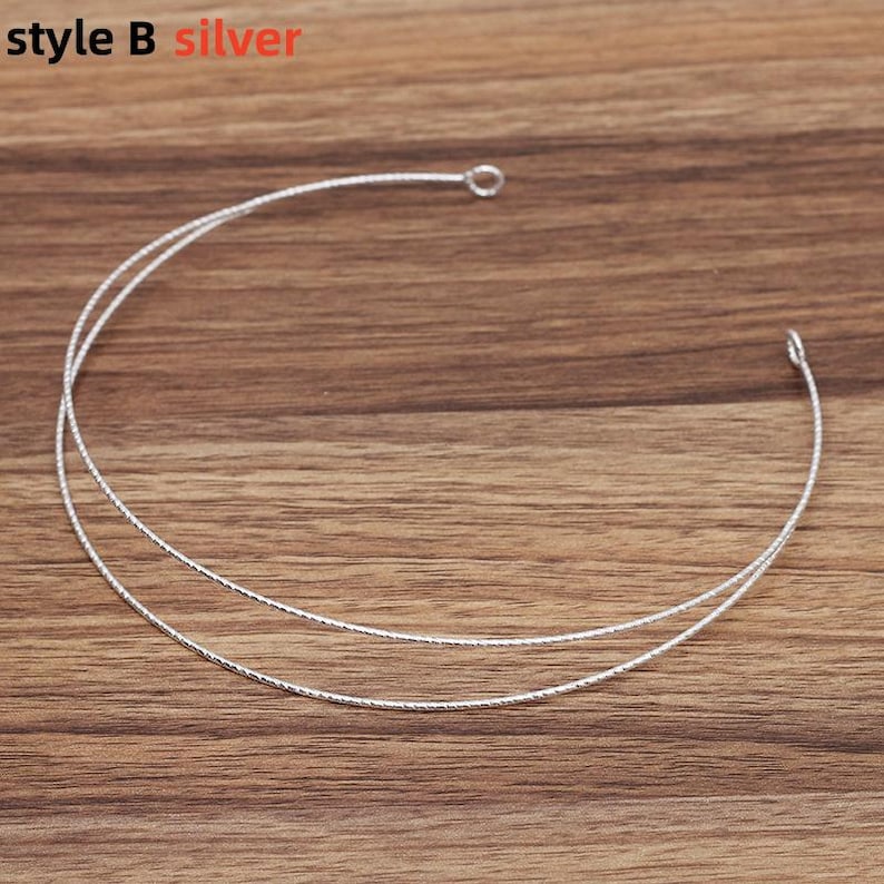 May include: Silver-colored necklace with two delicate strands, each with a textured surface. The necklace has a small loop at one end and a hook at the other. The text "style B silver" is in the upper left corner.