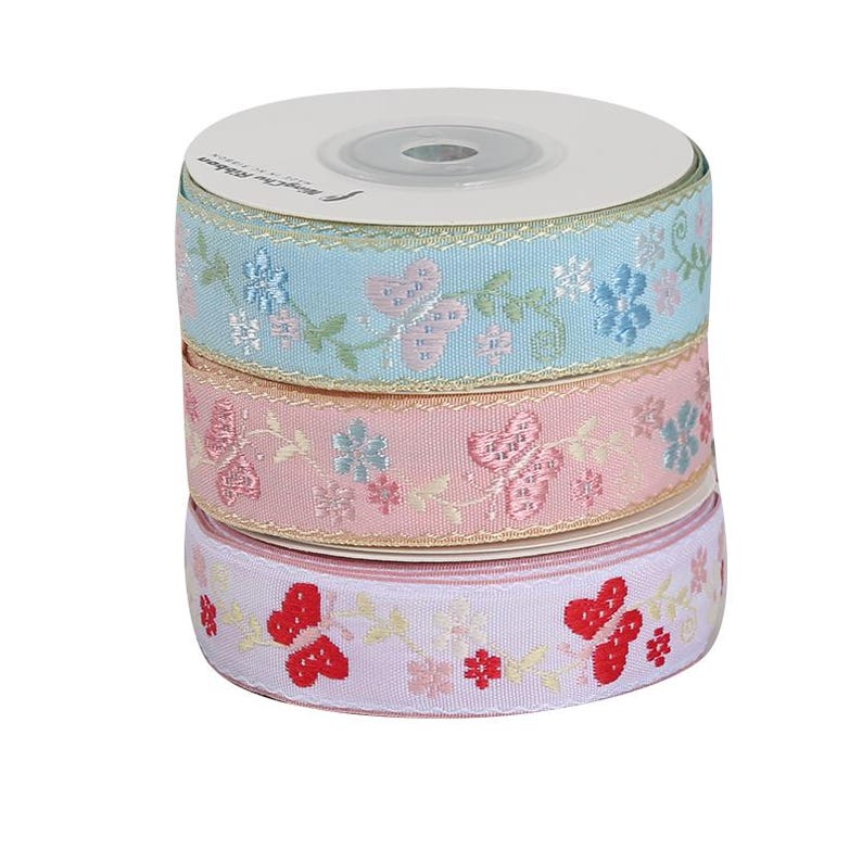 May include: A stack of three spools of decorative ribbon. The top spool is light blue with embroidered butterflies and flowers. The middle spool is pink, and the bottom spool is lavender with red butterflies.