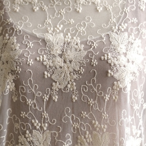 May include: White lace fabric with a delicate floral pattern. The lace is sheer and has a soft, romantic feel.