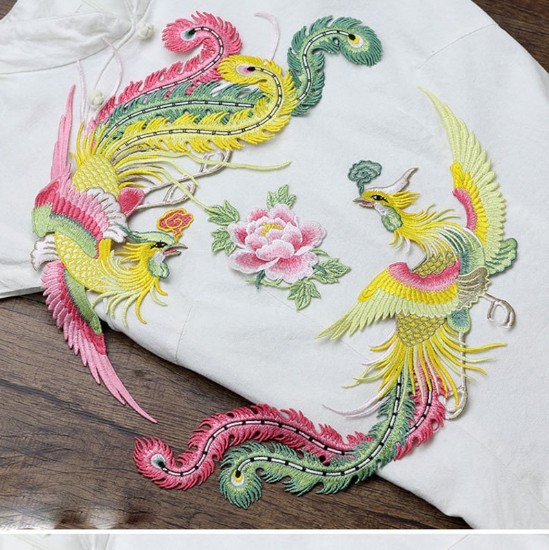 Op de afbeelding: Drie geborduurde strijkbare patches met een roze bloem en twee gele, groene en roze feniksen.