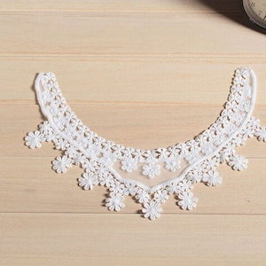 Puede incluir: Borde de encaje blanco con un borde festoneado y un diseño floral. El encaje es delicado e intrincado, con un toque suave y femenino.