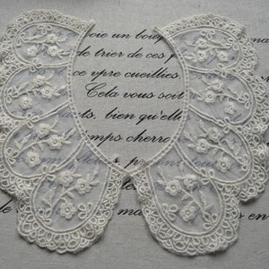 Puede incluir: Collar de encaje blanco con borde festoneado y bordado floral. El collar está hecho de tela delicada y tiene un aspecto vintage.