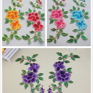 Op de afbeelding: Vijf geborduurde bloemenapplicaties in verschillende kleuren, waaronder geel, roze, blauw en paars. Elke applicatie heeft een bloemmotief met gouden accenten.