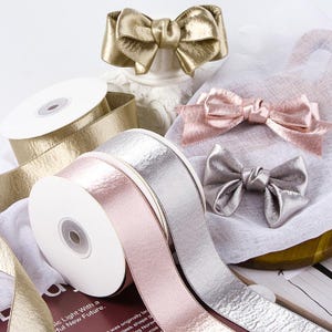 Puede incluir: Carretes y lazos de cinta metálica en oro, plata y rosa. La cinta tiene un aspecto texturizado. Los lazos están preatados. La imagen también muestra un carrete de cinta blanca.