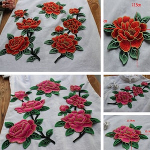 Könnte beinhalten: Zwei Sätze gestickter Blumenapplikationen. Ein Satz ist rot mit grünen Blättern und der andere ist rosa mit grünen Blättern. Jeder Satz ist etwa 12,5 cm breit und 15,5 cm lang.