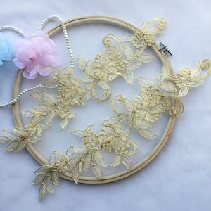 Könnte beinhalten: Vier goldene florale Spitzenapplikationen auf einem hölzernen Stickrahmen. Die Spitze ist zart und weist komplizierte Blumenmuster auf.