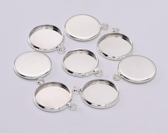 May include: A selection of silver-coloured, round bezel pendant trays, each with a small loop for attaching to a chain or other jewellery component. The trays have a shallow, recessed area for holding a cabochon or other decorative element.