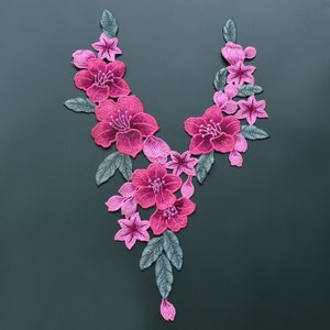 Könnte beinhalten: Rosa und grüne gestickte Blumenapplikation mit V-förmigem Design. Die Applikation zeigt eine Vielzahl von rosa Blüten mit grünen Blättern.