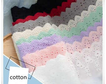May include: A stack of different coloured cotton lace trims with scalloped edges. The lace trims are arranged in a rainbow pattern, with the darkest colours at the bottom and the lightest colours at the top. The lace trims are all made of cotton and have a delicate, feminine look.