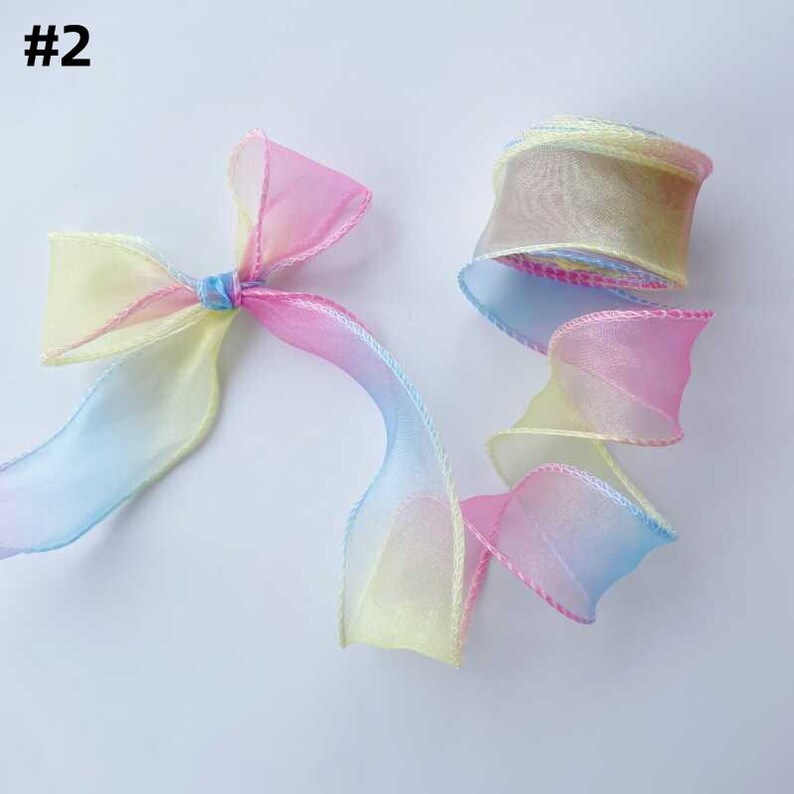 May include: A roll of pastel rainbow-colored ribbon with a matching bow. The ribbon is a gradient of yellow, pink, and blue. The ribbon is sheer and has a delicate, airy appearance. The number "#2" is in the top left corner.