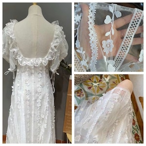 Może przedstawiać: Biała sukienka z koronki z kwadratowym dekoltem, krótkimi bufiastymi rękawami i falującą spódnicą. Sukienka ma delikatny wzór kwiatowy i koronkową lamówkę.