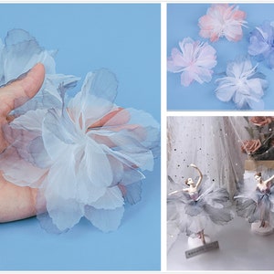 Könnte beinhalten: Eine Hand hält eine große, weiße Tüllblume mit einer geschichteten, zarten Textur. Die Blume besteht aus mehreren Schichten aus durchsichtigem Stoff, wodurch ein weicher und luftiger Look entsteht.