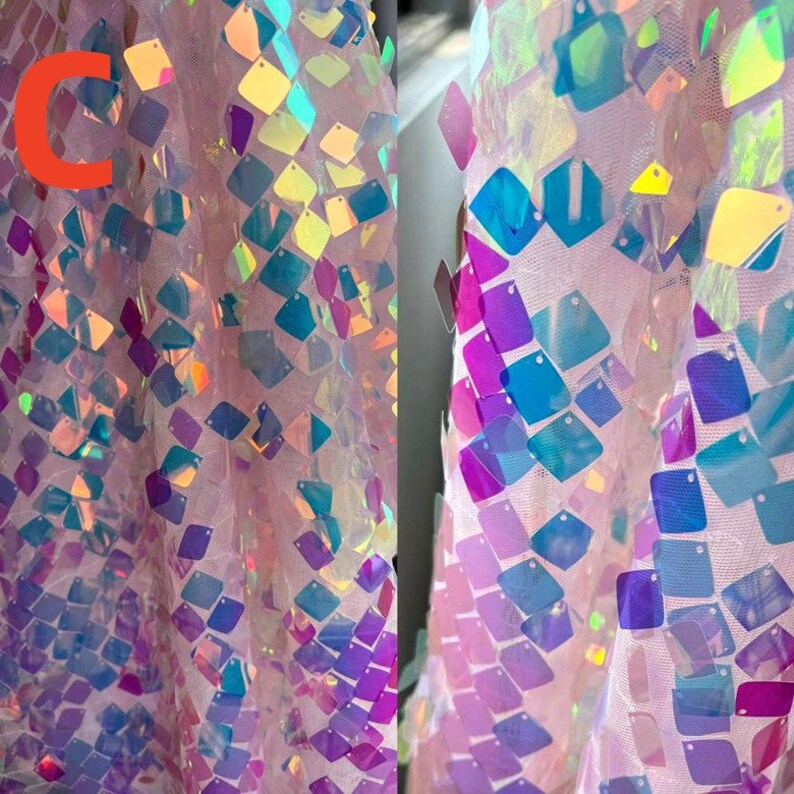 May include: Close-up of a pink fabric covered in iridescent square sequins. The sequins reflect a range of colors, including blue, purple, and yellow. The fabric has a sheer, net-like appearance.