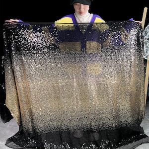Peut inclure: Un grand morceau de tissu avec un dégradé de paillettes dorées et noires. Les paillettes sont densément tassées, créant un effet scintillant. Le tissu est maintenu, mettant en valeur toute sa largeur et la transition de l'or au noir.