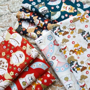 Puede incluir: Una pila de telas estampadas con dise&ntilde;os de inspiraci&oacute;n japonesa. Las telas muestran patrones repetidos de perros Shiba Inu, abanicos y motivos florales en rojo, azul marino y blanco. Las telas est&aacute;n dobladas y apiladas sobre una superficie de encaje.