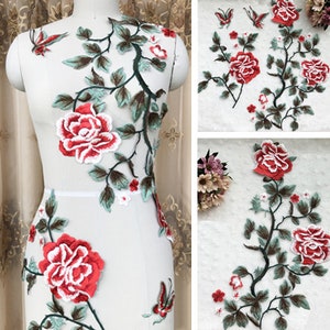 Könnte beinhalten: Florale Stickerei Applikation mit roten und weißen Rosen, grünen Blättern und Schmetterlingen. Die Applikation ist auf einem weißen Netzstoff.