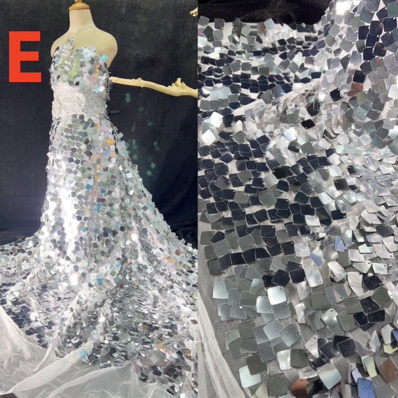 May include: A strapless, floor-length gown covered in silver square sequins. The dress is displayed on a mannequin and has a fitted bodice that flares into a full skirt. The fabric is also shown separately, revealing the sequin pattern.
