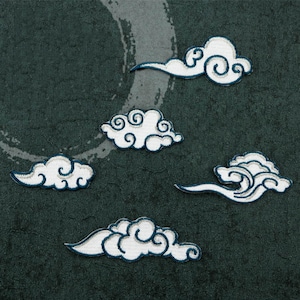May include: Five white embroidered cloud patches with blue outlines on a dark green fabric background.