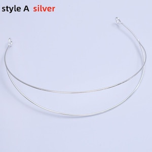 May include: A silver-colored metal headband with two parallel arcs. The text "style A silver" is in the top left corner. The headband has small loops at each end. The background is a solid light color.