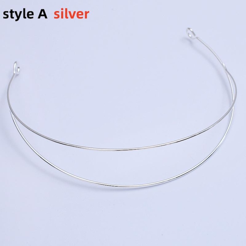 May include: A silver-colored metal headband with two parallel arcs. The text "style A silver" is in the top left corner. The headband has small loops at each end. The background is a solid light color.