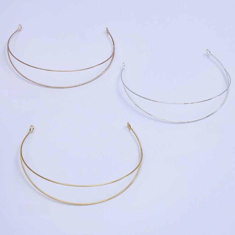 May include: Three minimalist necklaces in gold, silver, and rose gold. Each necklace features a double-layered, curved design with small loops at the ends. The jewelry is displayed on a plain white background, highlighting the simple elegance of the pieces.