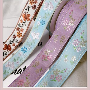 May include: Close-up of four decorative ribbons with floral and butterfly patterns. The ribbons are in shades of orange, light blue, and purple. The ribbons are likely used for crafts, gift wrapping, or embellishments.