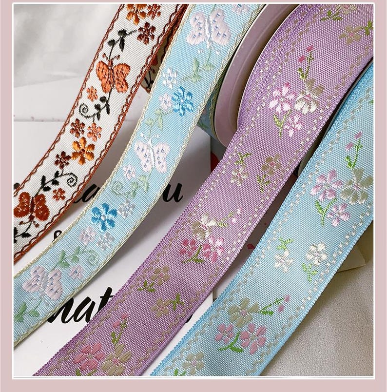 May include: Close-up of four decorative ribbons with floral and butterfly patterns. The ribbons are in shades of orange, light blue, and purple. The ribbons are likely used for crafts, gift wrapping, or embellishments.