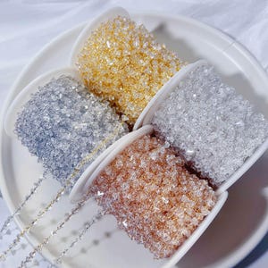 Puede incluir: Cuatro carretes de cadena de cuentas en colores oro, plata y oro rosa. Las cuentas son pequeñas, facetadas y ensartadas. Los carretes están dispuestos sobre un plato blanco poco profundo.