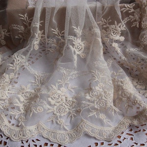 May include: White lace fabric with a delicate floral pattern. The lace has a scalloped edge and is perfect for adding a touch of elegance to any project.