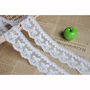 Puede incluir: Borde de encaje blanco con un borde festoneado y un patrón repetitivo de pequeños lazos. El encaje es delicado e intrincado, y sería perfecto para agregar un toque de elegancia a cualquier proyecto.