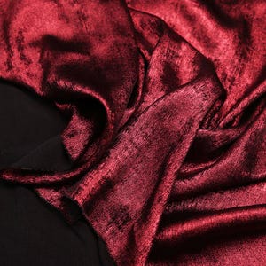Pode incluir: Close-up de um tecido vermelho escuro com um brilho met&aacute;lico. O tecido est&aacute; dobrado e drapeado, mostrando sua textura e brilho.