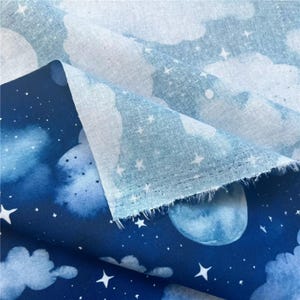 May include: Blue cotton fabric with a white and blue watercolor print of clouds and stars. The fabric is folded in half, showing the back side of the fabric.