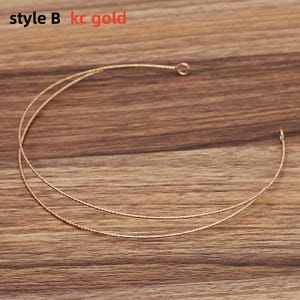 May include: A delicate gold-colored necklace with a double-strand design. The necklace has a textured appearance and is displayed on a wooden surface. The text "style B kc gold" is visible in the upper left corner.