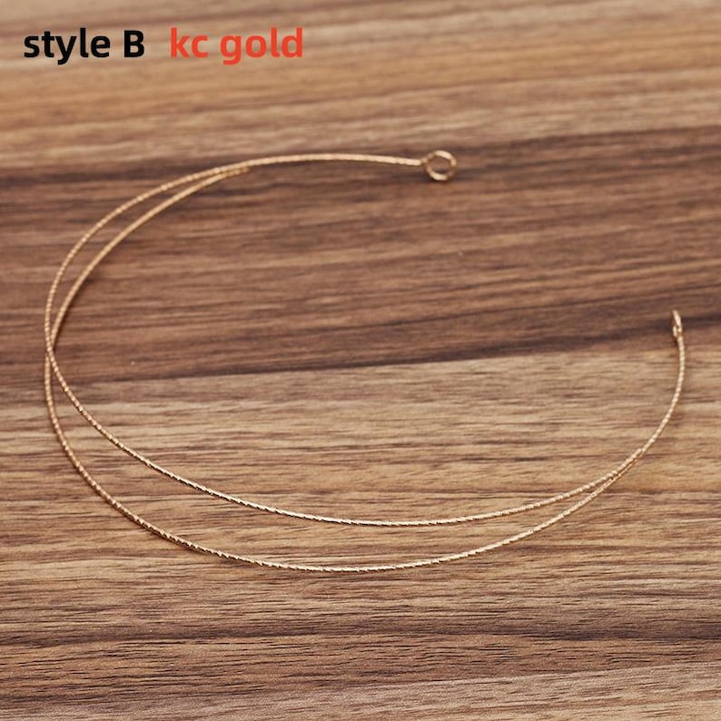 May include: A delicate gold-colored necklace with a double-strand design. The necklace has a textured appearance and is displayed on a wooden surface. The text "style B kc gold" is visible in the upper left corner.