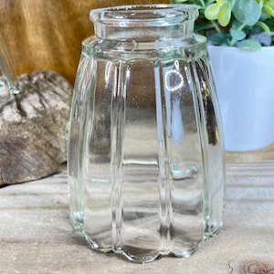 May include: Clear glass jar with a fluted, scalloped design. The jar has a wide opening and a slightly flared rim. The glass is transparent, allowing a view of the contents. The jar is likely used for storage or display.