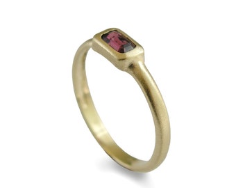 May include: A gold ring with a rectangular, dark pink gemstone set in a bezel setting.