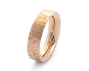 May include: A rose gold band ring with a textured finish. The ring is simple and elegant.
