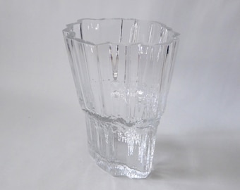 May include: A clear glass vase with a textured, ridged design. The vase has a unique shape with a jagged top edge and a textured lower portion. The vase is made of clear glass and is suitable for displaying flowers or as a decorative piece.