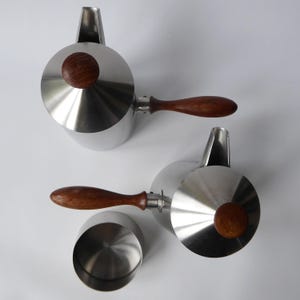 May include: Two stainless steel teapots with wooden handles and lids. The teapots have a polished finish and a modern design.