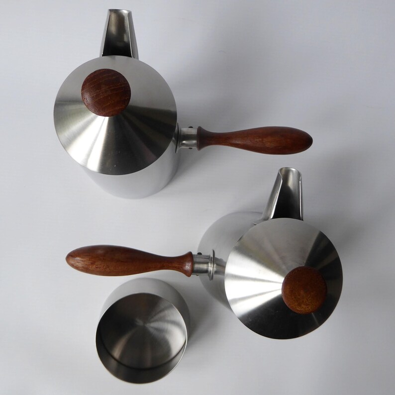 May include: Two stainless steel teapots with wooden handles and lids. The teapots have a polished finish and a modern design.