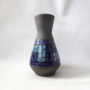 May include: A ceramic vase with a dark grey, textured body and a flared top. The middle section features a mosaic pattern in shades of blue and turquoise. The vase has a rounded base and a narrow neck.