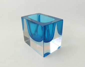 Könnte beinhalten: Eine rechteckige Glasvase mit einem dicken, klaren Boden und einem leuchtend blauen Innenraum. Das Design besteht aus einem massiven Block aus transparentem Glas mit einer tiefen, abgerundeten blauen Vertiefung in der Mitte der Oberseite.