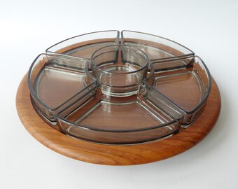 Könnte beinhalten: Ein Vintage-Serviertablett mit Holzsockel und transparenten Glasfächern. Das Tablett hat einen kreisförmigen Holzsockel mit einer zentralen runden Glasschale und fünf umliegenden Glasabschnitten, ideal für Snacks oder Vorspeisen.